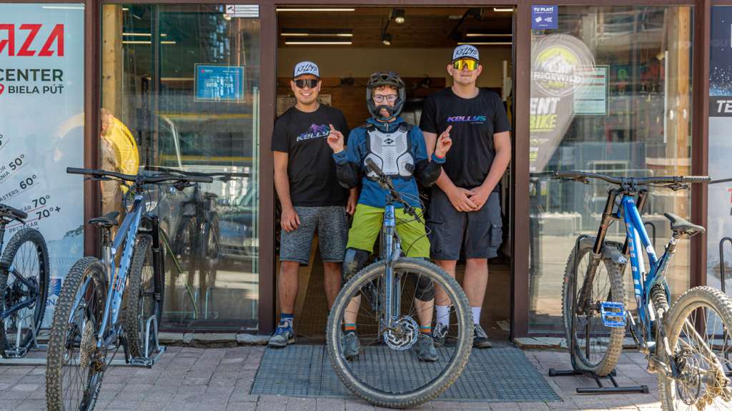 Cyclist wearing protective gear posing with two members of staff outside Rental Bike Park Jasná