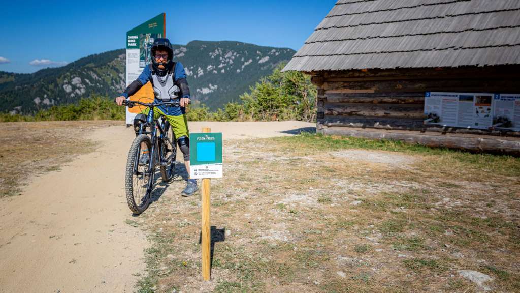 Cyclist at the start of the blue Flow trail beside a wooden log cabin