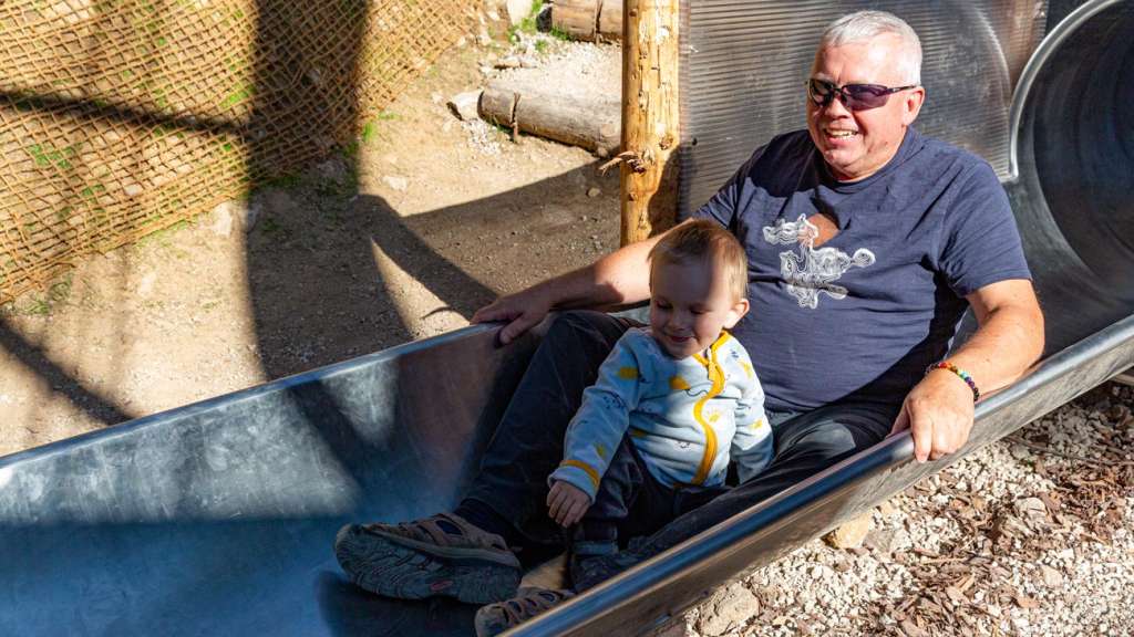 Grandfather and grandson sliding down a stainless-steel slide